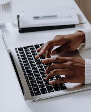 African American woman's hands typing on silver laptop with black keys