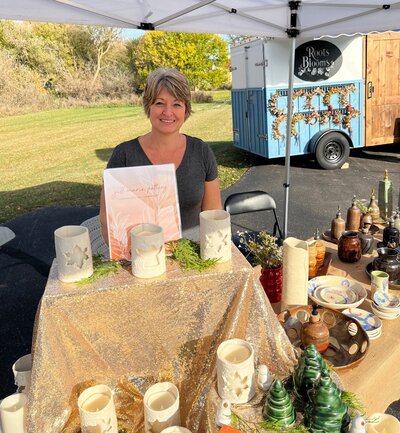 Jill stands beside a table of her handmade ceramic holiday decorations at a vendor fair in Laingsburg, MI