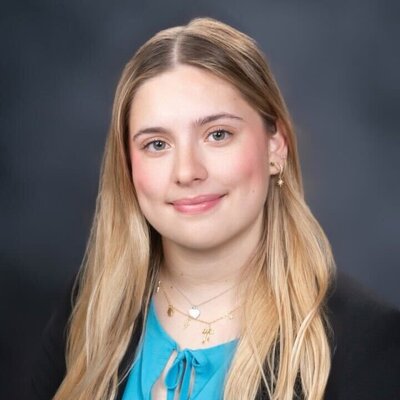 Woman with blond hair wearing black blazer and blue shirt smiling at camera