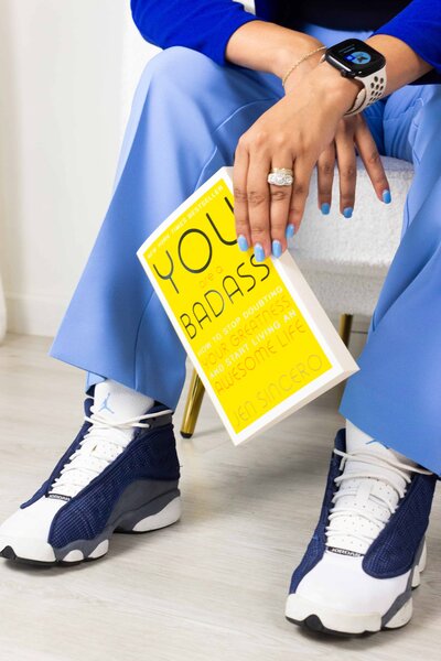 Bilingual coach promoting career confidence, holding a yellow children’s book and wearing blue sneakers