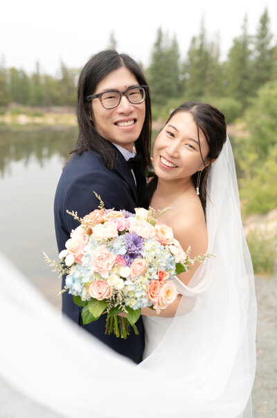 Bride and Groom leaning in towards the camera and smiling with veil swooping frame of photo during their elopement day in Colorado Springs