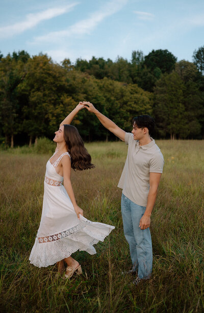 In the enchanting moments of their engagement session, a couple gracefully twirls in a dance amidst a scenic field.