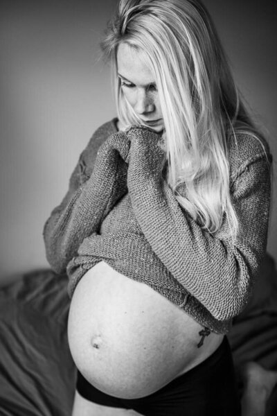 A black and white image of an expecting mother showing off her growing belly during an in home maternity session with Kate Simpson.