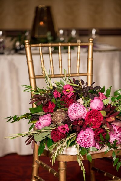 Large pink and maroon bridal bouquet sitting on a gold chaivari chair