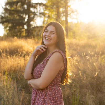 Senior girl with brown hair and brown eyes laughing in field at sunset at Flaming Geyser State Park senior photos she has an infectious laugh and smile