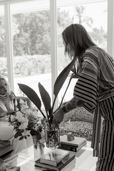 Black and white branding photo showing a woman arranging flowers on a coffee table during a branding shoot. Greenville SC. Dani Lacey Photographs.
