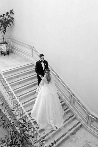 Bride and groom meet in the middle of elaborate staircase on their wedding day