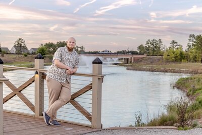 A Cape Fear Community College senior leaning on a wooden bridge by a scenic lake at sunset in North Carolina. This relaxed portrait captures the essence of professional senior photography, ideal for those seeking natural and serene photos in Wilmington.