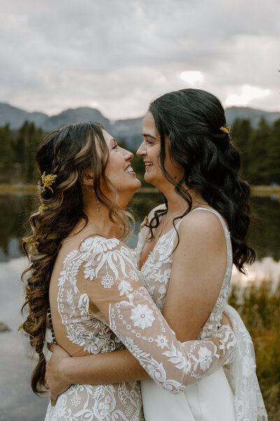 two brides kissing while standing next to a lake with mountains in the background