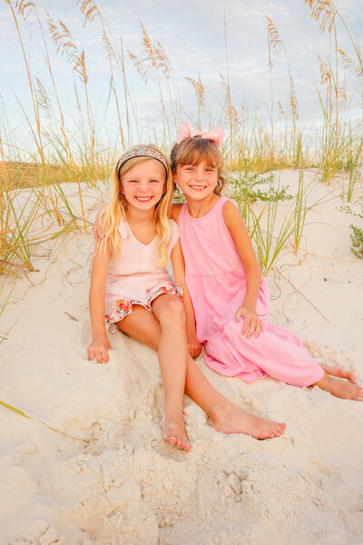 2 girls giggle in a fun pose on a sand dune with seaoats in the background