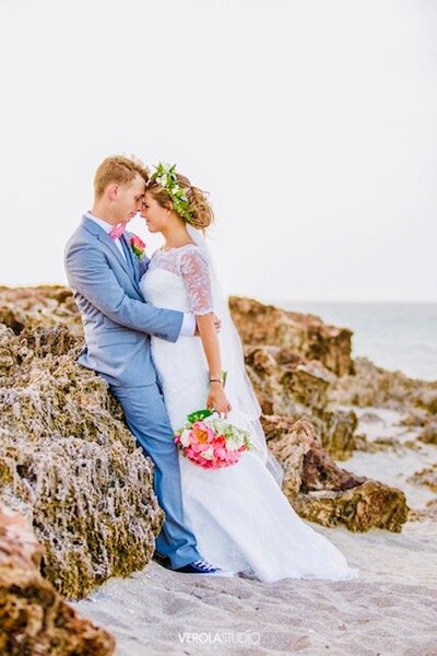 Bride and groom leaning on rocks at beach
