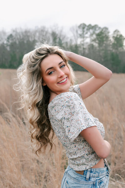 high school senior smiling and playing with her hair and posing for senior photographer in raleigh nc