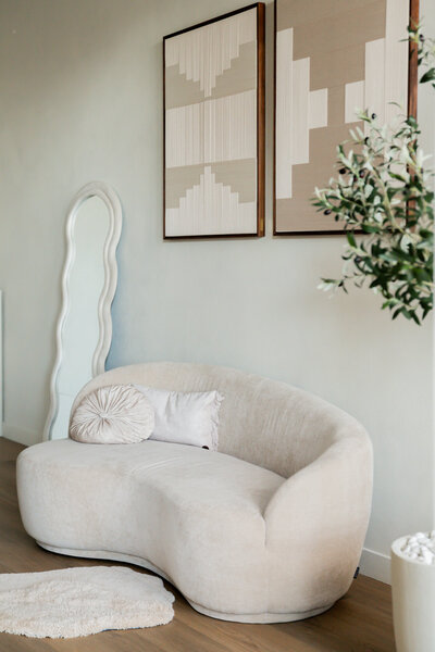 Sfeervolle zithoek in Studio Laurant met een organische sofa, twee handgemaakte kunstwerken en een spiegel, voor een elegante en artistieke uitstraling.