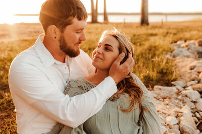 little rock engagement photography with man sitting behind a woman and holding her hair back as he gazes into her eyes at a sunset session in little rock