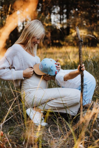 Mutter und Sohn zusammen in der Natur, Sohn gibt dem Babybauch der Mutter einen Kuss