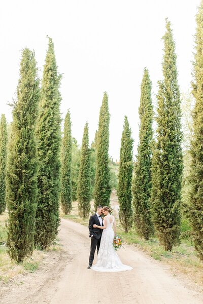 Italian inspired wedding with Bride and groom standing between trees at Milagro Winery in Ramona, California.