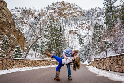 Engaged couple doing a dip on a bridge with cliffs behind them during their winter engagement session in Cheyenne Cañon, Colorado Springs.