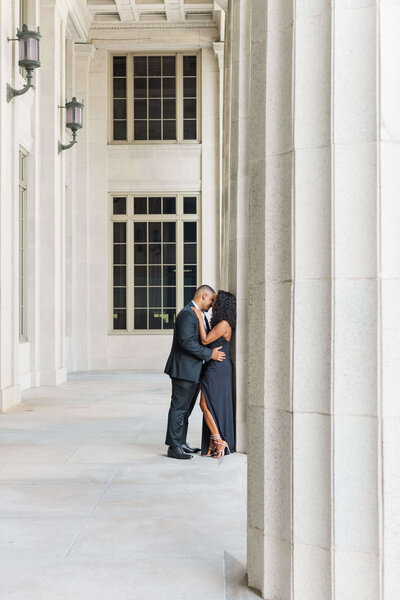 a couple stanting while kissing against a white column