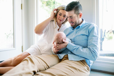 Mom and Dad gazed at their newborn son while sitting on the floor with sunlight coming in the window.