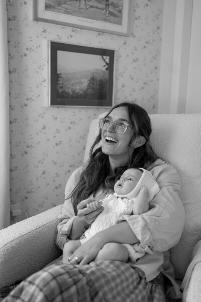 Mom sitting in chair holding baby while laughing for east coast photography session
