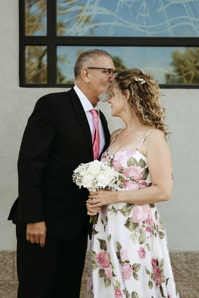 Photo of a man kissing a woman on the forehead at a vow renewal.
