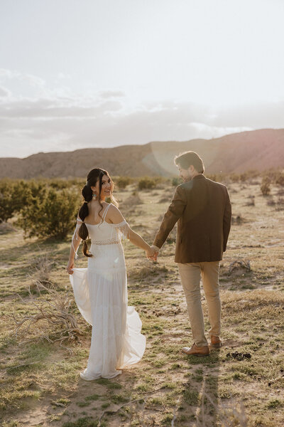 bride and groom walking with horses with desert mountains in the background