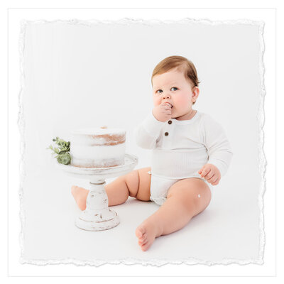 One-year-old boy at cake smash photo session captures an adorable and joyful moment. In this photo, the baby is dressed in an all-white romper, digging into a delicious-looking white cake in front of an all-white backdrop. Bri Sillvan captured the purity and simplicity of this image with her clean, classic image. It radiates happiness and brings a smile to the viewer's face because of the baby's infectious smile and the sweet setting.