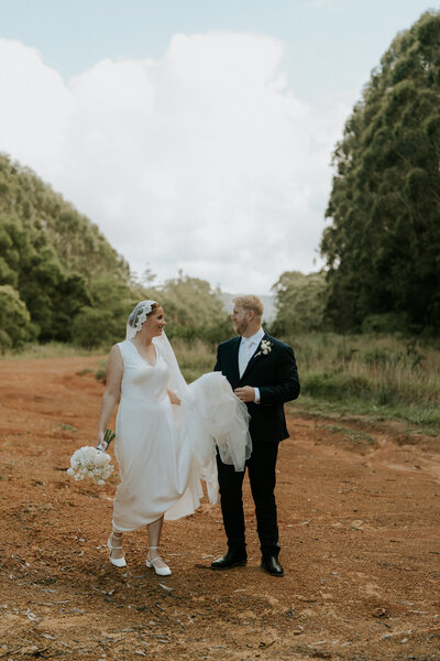 A candid photo of a Sawtell wedding couple during their portrait session. She is holding her dress. They are out in nature.