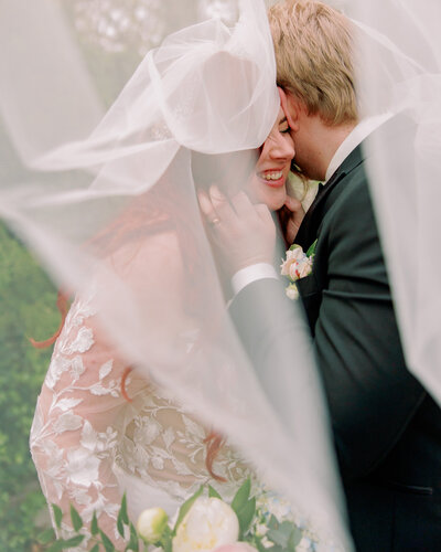 Newlyweds kiss, a veil surrounding them.