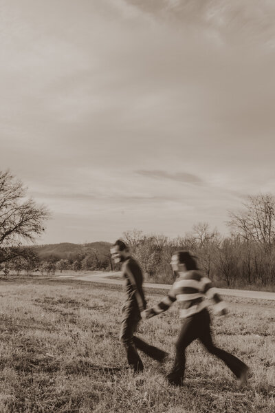 Engaged couple running in a field of grass captured by a Minnesota couples Photographer