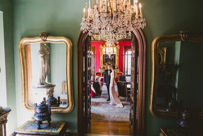 Formal bride and groom stand in the luxe and moody paramour estate salon for their first look photos.