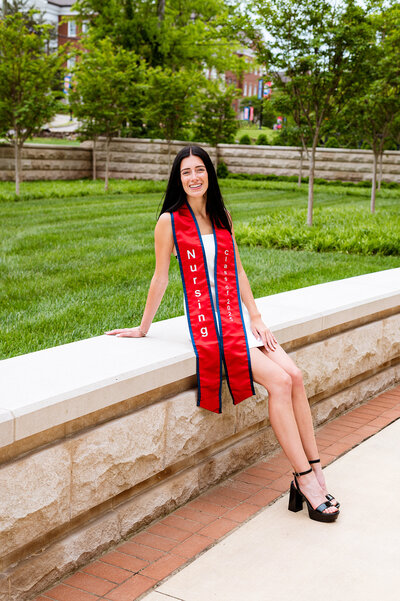 Belmont senior wearing red nursing school stole and sitting on the banister outside the medical college