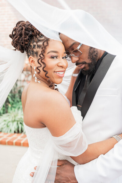 A wedding couple standing close together under a veil