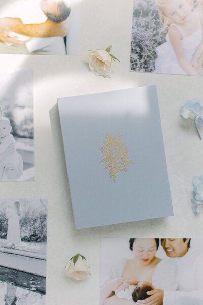 A flatlay image of a linen photo box surrounded by loose prints and small flower buds