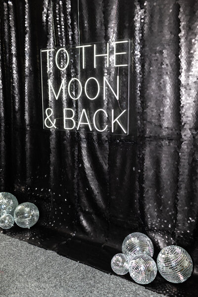 To the Moon and Back neon Sign hire for mad hat photo booth with a black sequins backdrop and disco balls for hire or rent in the Cotswolds, Oxford, Bristol and surroundings