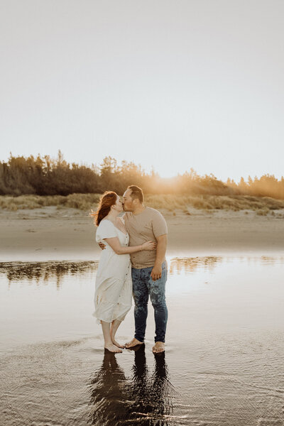 A couple kiss while the sun sets behind them and they're taking a moment to be photographed during a family photoshoot as just the adults in christchurch