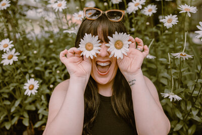 woman holding daisy flowers over her eyes