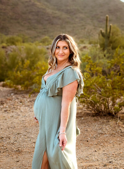 beautiful mom-to-be holding her baby bump and playing with her gown in Arizona