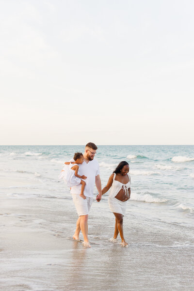 Photographer captures pregnant couple walking along the beach during their maternity photo session