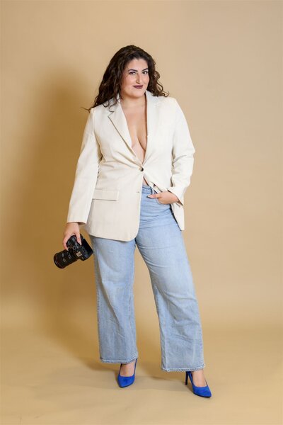 Hiba, Raleigh wedding photographer and videographer, holding a camera during personal branding photo session on tan backdrop.