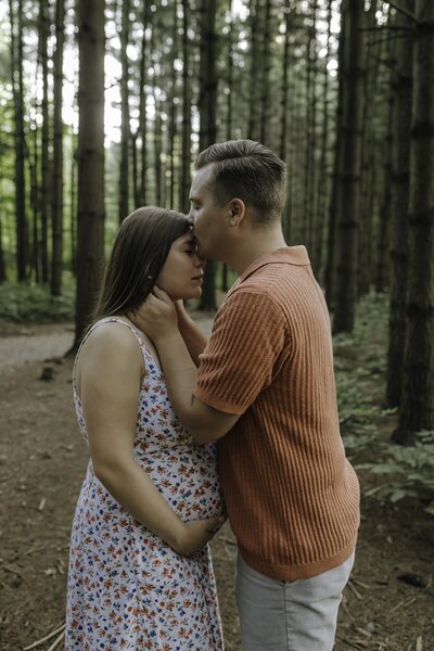 Verona B Photography captures a maternity photoshoot of a man kissing his wife on the forehead while she holds her pregnant belly. The picture is intimate and peaceful in this woodsy setting at Silver Creek Metro Park.