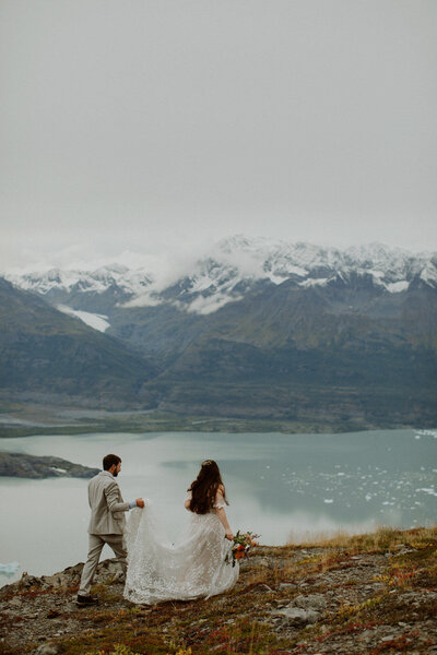 Bride and groom walk along an overlook, above a glacial lagoon in Alaska