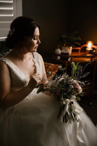A bride being lit by the light coming from a window on one side holding her wedding bouquet while posing for her bridal portraits with new plymouth photographer aimee kelly