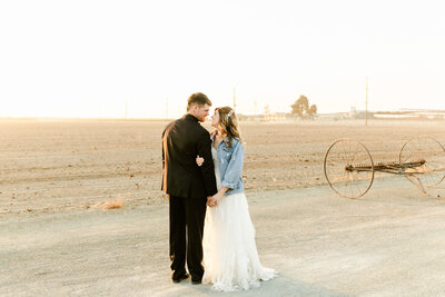 bride in jean jacket with groom by open field rustic