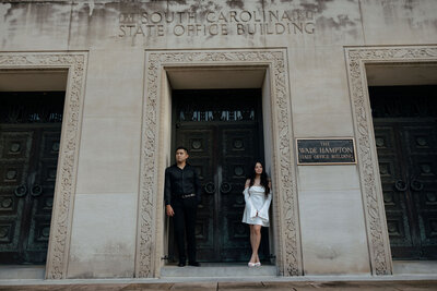 A couple stands on opposite sides of an ornate doorway on the South Carolina State House grounds. They are looking away from each other adding to the moody vibe.