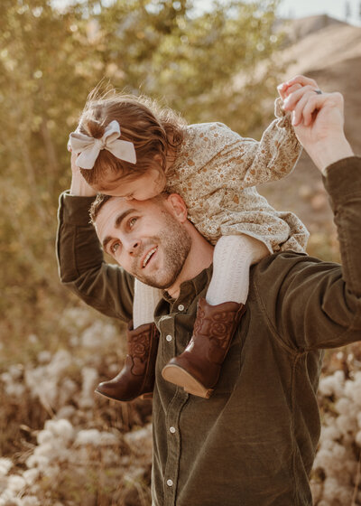 father holding daughter on shoulders and smiling