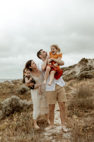 A relaxed family photography session in Perth, featuring a joyful moment as parents share laughter with their two young children in a natural beach setting.