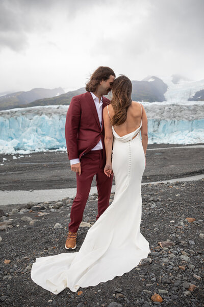 Bride and groom stand shoulder to should with their foreheads resting against each other in front of a glacier in Alaska.