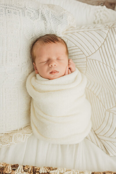 newborn boy swaddled in blue with a blue bonnet sleeping peacefully on a plaid blue mattress and tiny metal bed