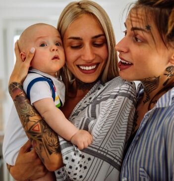 Two mothers holding and interacting with their baby.